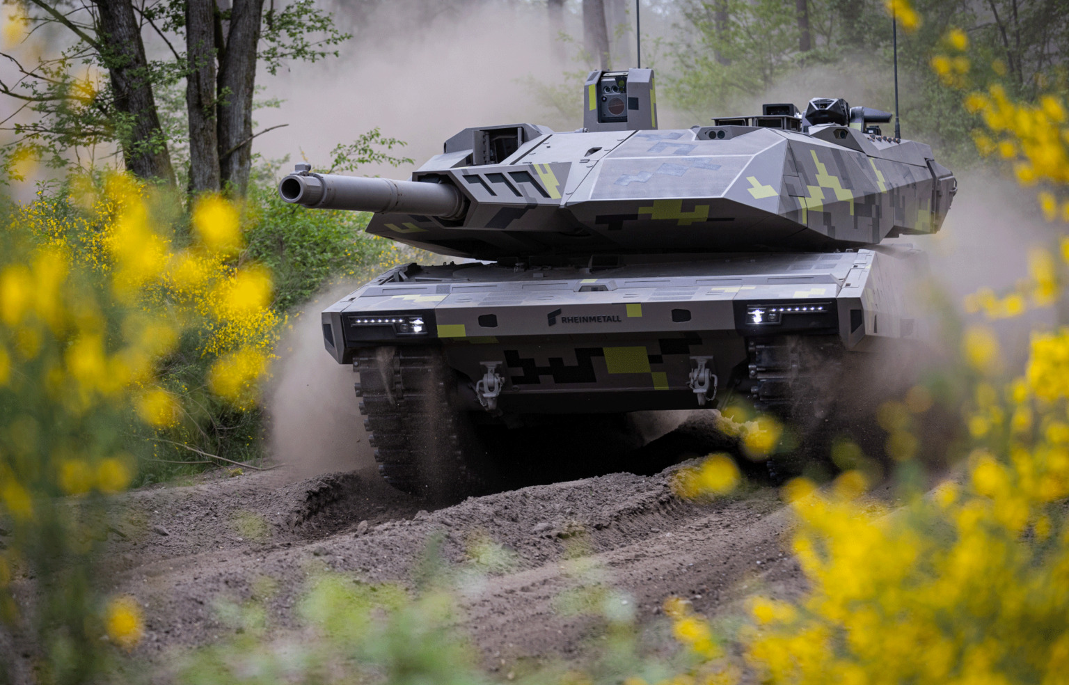Char Panther KF51 de Rheinmetall en mouvement sur une piste forestière, camouflage pixelisé gris et jaune, canon pointé vers la gauche