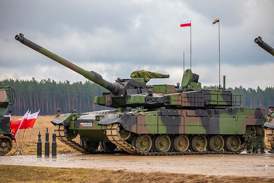 Char K2 de l’armée polonaise en démonstration statique sur un champ de tir boueux, canon relevé, drapeaux polonais à ses côtés