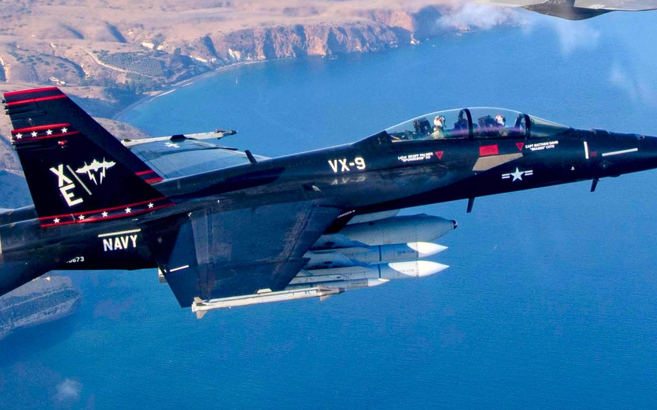 Chasseur embarqué américain en livrée noire d’escadron d’essais, emportant sous son aile deux missiles air-air de grande taille au-dessus du Pacifique