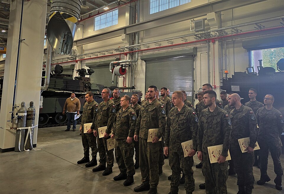 Militaires polonais alignés avec leurs certificats dans un atelier de maintenance, un char américain stationné derrière eux