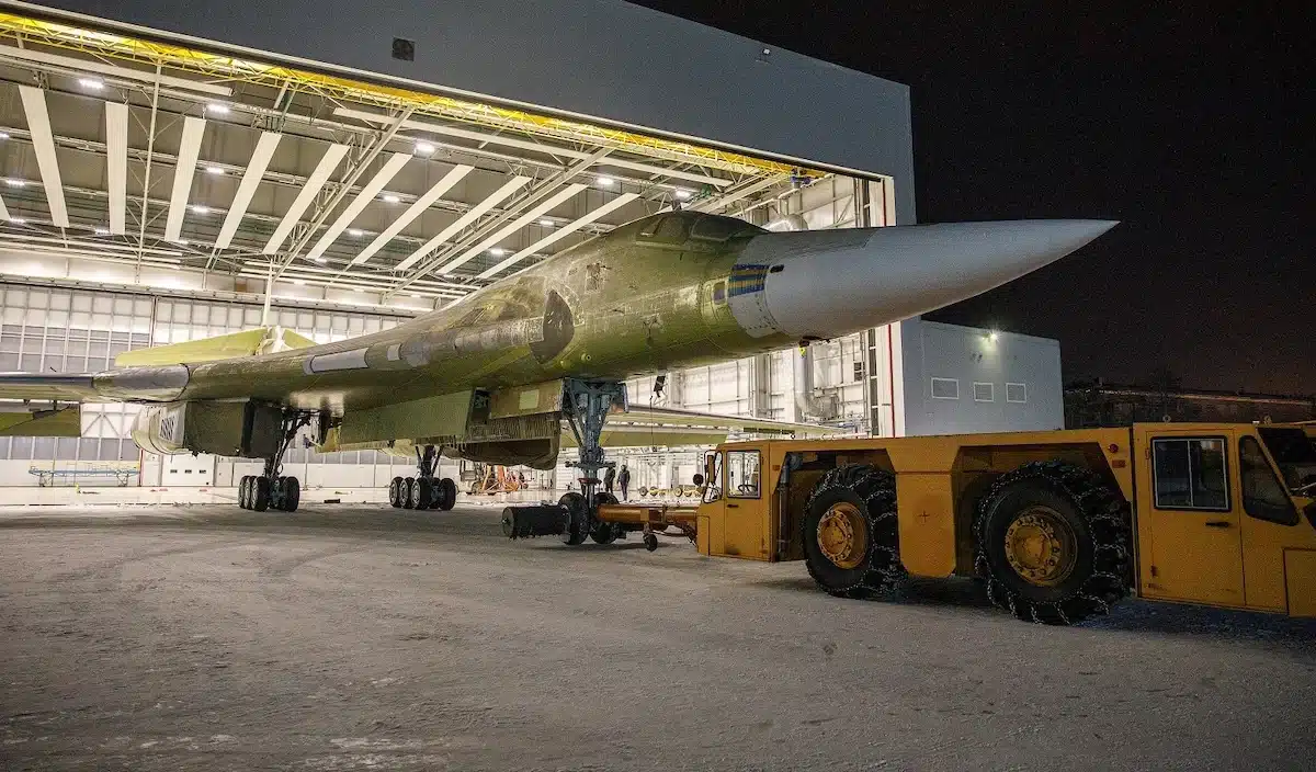 Un bombardier stratégique encore en apprêt vert tracté hors d’un hangar d’assemblage, de nuit